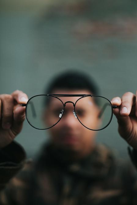 A person holding a pair of black glasses in front of a blurred background.