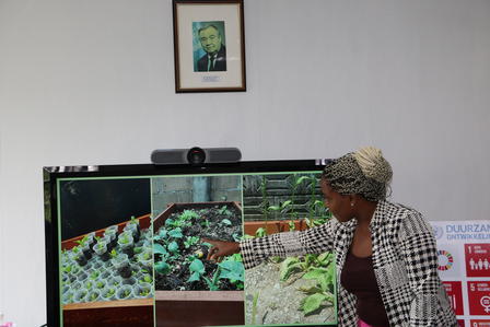 A woman gestures towards a digital display featuring various plants and gardening images.