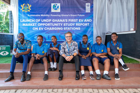 Group of six people, including students and a man in a shirt, seated in front of a banner.