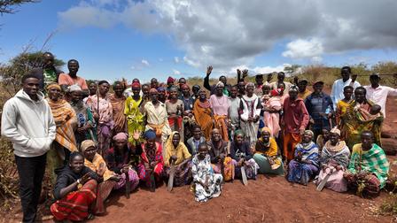 A large group of people of various ages and attire posing together outdoors under a blue sky.