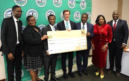 Group of six people holding a large check, smiling, in front of a branded backdrop.
