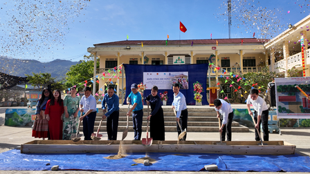 A group of people participating in a ceremony outdoors, with decorations and a building in the background.
