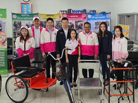 Group of six people in matching pink jackets posing with mobility aids in a showroom.