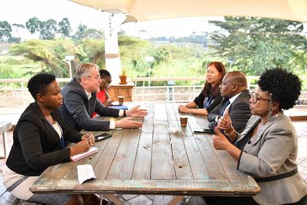 A diverse group of six people engaged in a discussion around a wooden table outdoors.