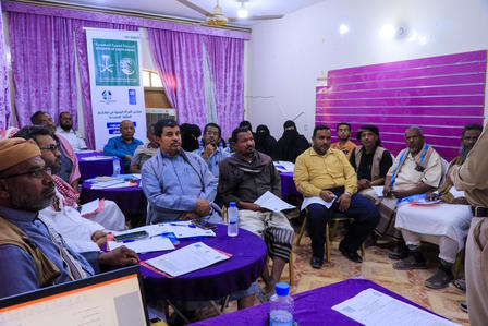 A group of people sitting in a brightly lit room, engaged in a discussion or presentation.