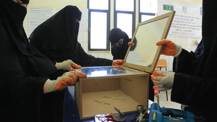Women in black abayas assembling a reflective box in a classroom setting.
