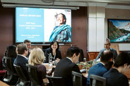 A group of professionals seated around a conference table with a presentation screen in the background.