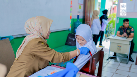 A healthcare worker administers a vaccination to a young girl in a classroom setting.