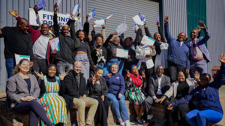 A diverse group of people celebrating together, holding certificates and smiling outdoors.