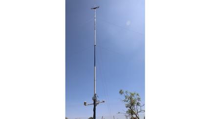 A tall communications tower against a clear blue sky, with plants at the base.