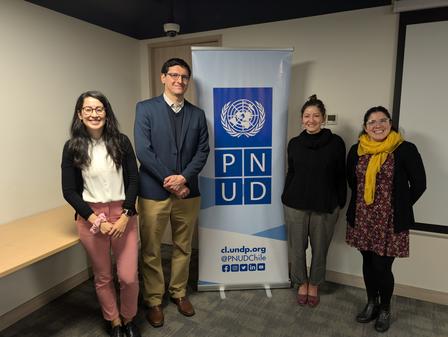 Four professionals pose together in front of a banner with the PNUD logo in an indoor setting.