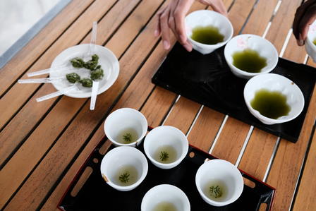 Two trays with small bowls of green tea and tea leaves on a wooden table.