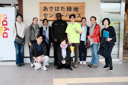A diverse group of ten people stands together, smiling in front of a wooden sign.