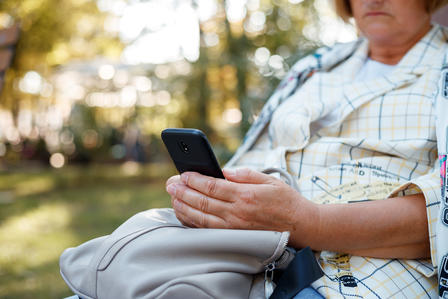 A close-up of a woman sitting outdoors, checking her smartphone with a relaxed expression.