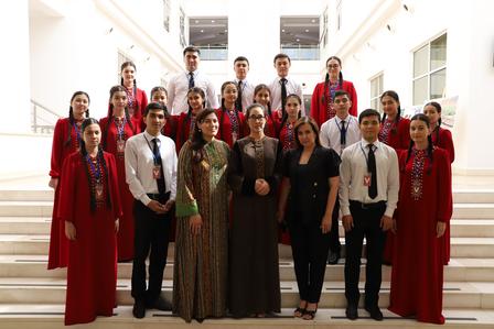 Group of individuals in formal attire, posing together on staircase in a bright interior.