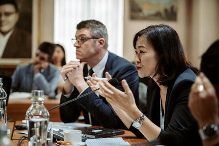 A woman speaks passionately during a meeting, with a man listening intently beside her.