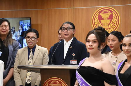 A group of people at a podium, with a man speaking and women in formal attire.