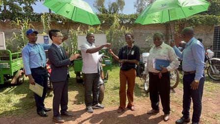 A group of people receiving keys and umbrellas during a vehicle handover event outdoors.