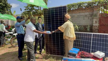 Four people engage in a solar panel donation event, with panels and equipment in the foreground.