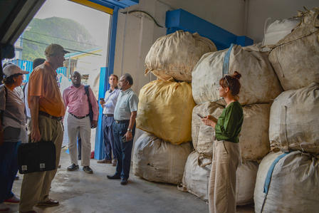 A group of people stands inside a warehouse, beside large, stacked bags.