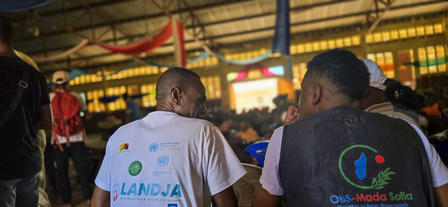 Two individuals in a busy indoor setting, engaged in conversation with backs to the camera.