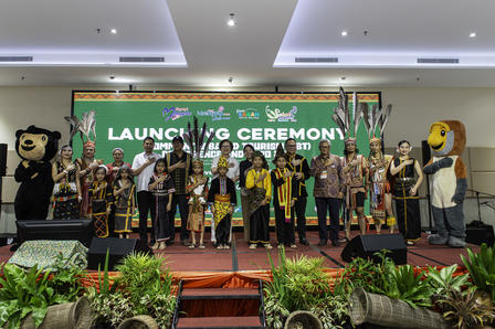 A vibrant launch ceremony with diverse participants holding instruments, surrounded by greenery.
