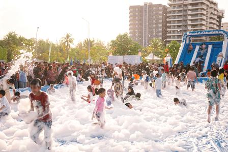 Children playing in a foam-filled area, with a slide and crowd in the background.