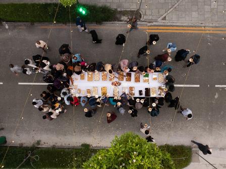 Aerial view of a long dining table set with food, surrounded by people on a street.
