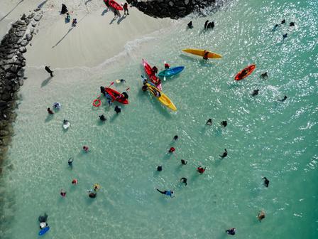 Aerial view of a beach with people swimming and kayaking in clear turquoise water.