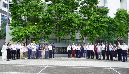 A large group of people posing together outdoors in front of a building and lush green trees.