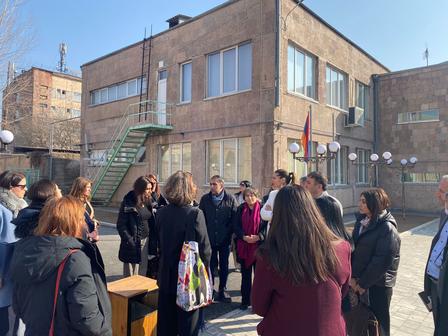 A group of people gathered outside a building, discussing in a sunny courtyard.