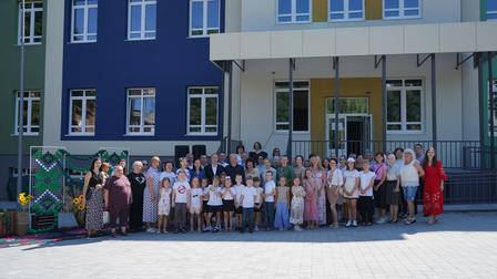 Group photo of diverse people in formal and casual attire outside a colorful building.