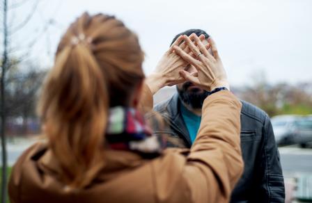 A woman with long hair gestures towards a man outdoors on a cloudy day.