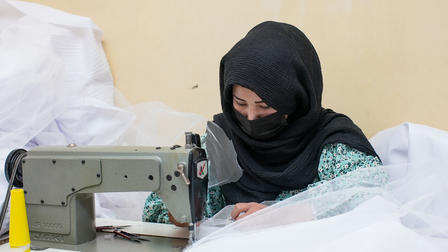 A woman in a black hijab focused on sewing with a machine amidst white fabric.