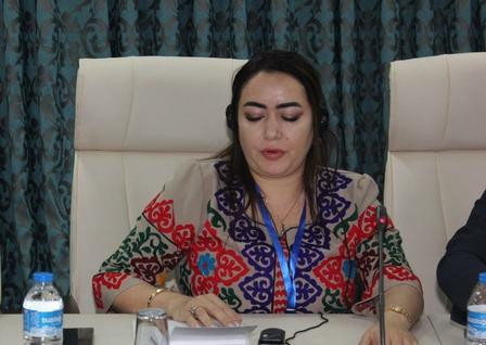 A woman wearing a colorful embroidered blouse speaks into a microphone at a conference table.