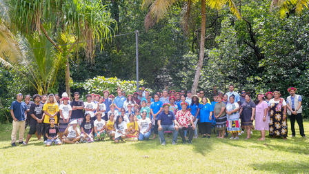 A large group of diverse people posing together in a sunny, green garden setting.