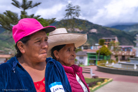 Two women, one in a pink cap and the other in a wide-brimmed hat, stand outdoors.