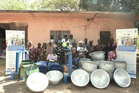 A diverse group of women stands proudly in front of a building, surrounded by cooking equipment.