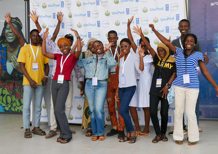 Group of young people celebrating with raised hands in front of a branded backdrop.