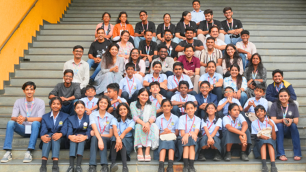 A large group of students and adults posing together on outdoor stairs, smiling.