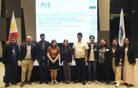 Group of professionals posing for a photo at a conference, with flags and a presentation backdrop.