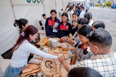 A group of people gather around a vendor displaying handmade crafts at an outdoor market.