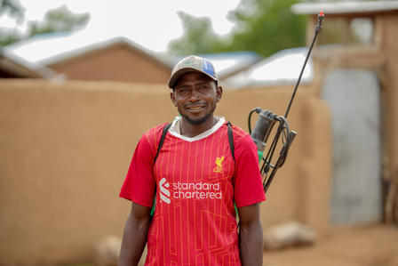 Smiling man in a red Liverpool jersey stands outdoors with buildings in the background.