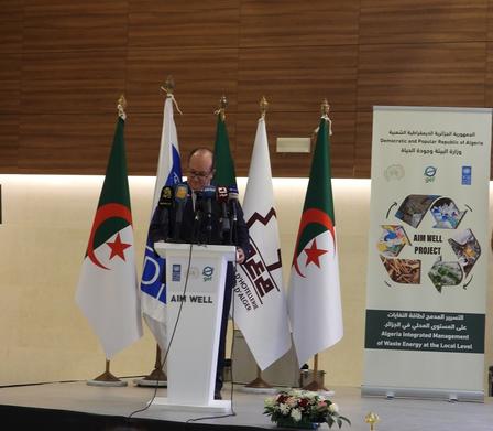 A speaker at a podium surrounded by flags, addressing an audience in a conference setting.