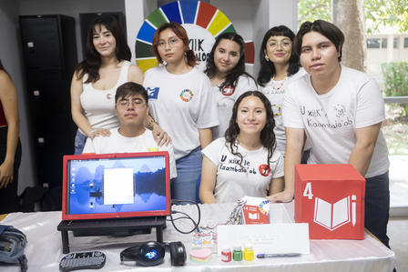 A group of seven people in white shirts pose at a table showcasing technology and exhibits.