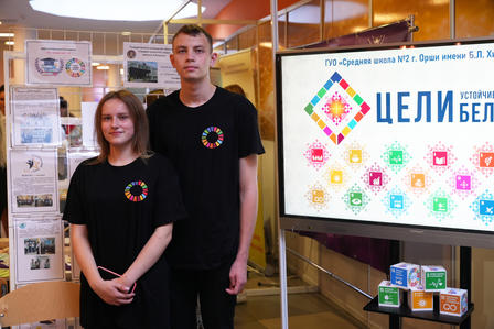 Two young adults in matching black t-shirts stand in front of a colorful display booth.