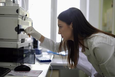 A focused woman in a lab coat operates a scientific instrument in a bright laboratory.
