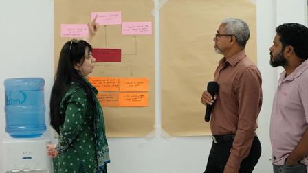 A woman points at a flowchart on paper while two men listen attentively.