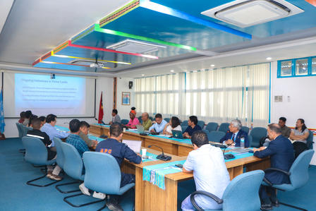 A conference room with attendees seated at a long table, discussing a presentation.