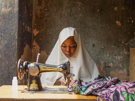 A young woman in a hijab sewing with a vintage sewing machine in a dimly lit room.